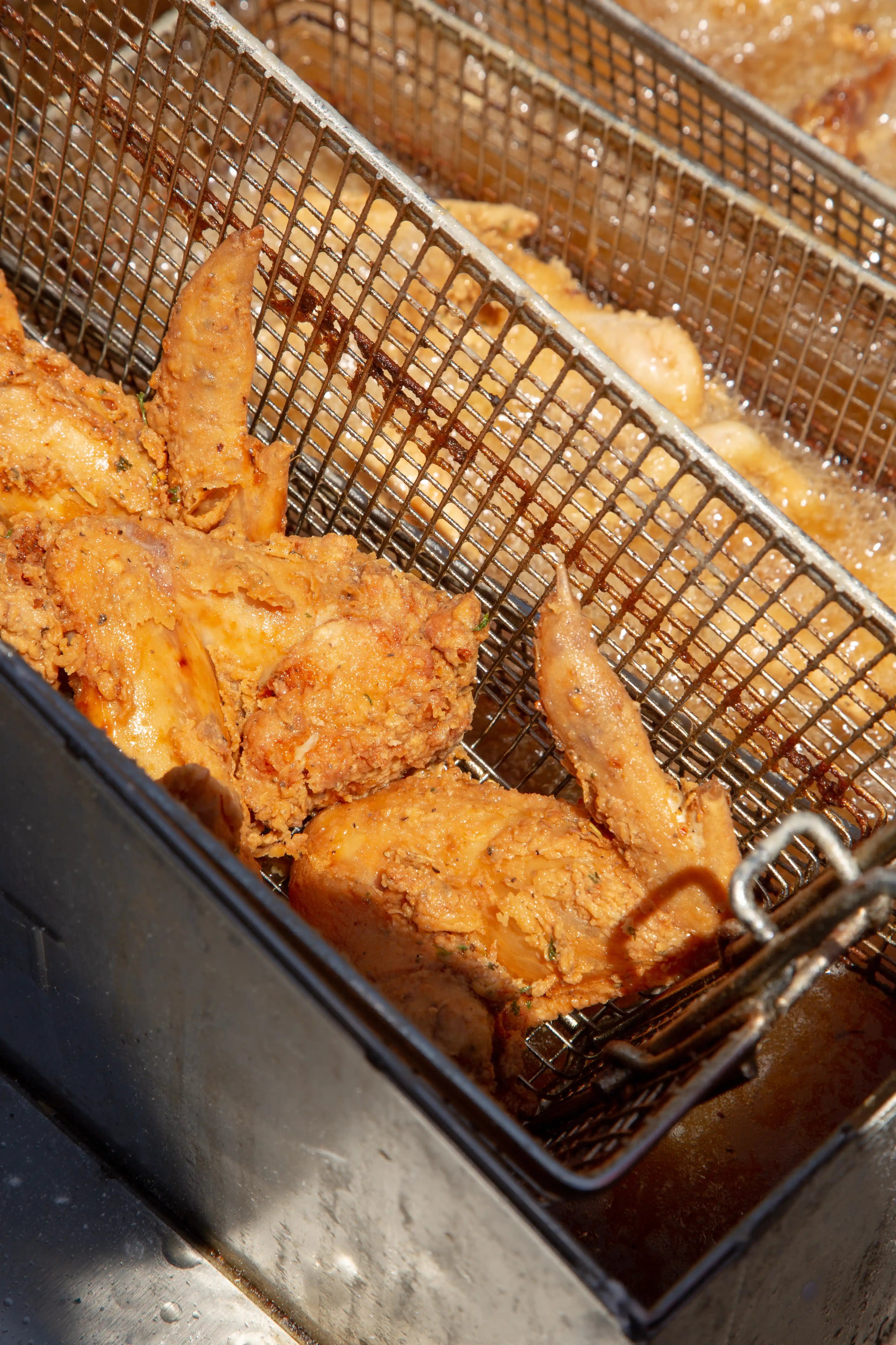 Freshly cooked golden crispy chicken wings in a stainless steel fryer basket, cooked using Tenshine commercial pressure fryer